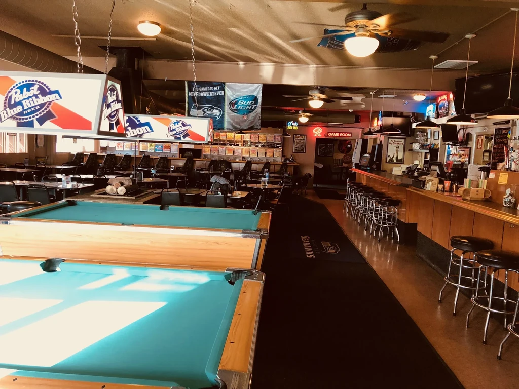 Empty sports bar interior featuring pool tables and Seahawks decor.