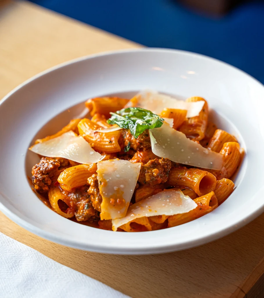 Close-up: Rigatoni pasta with meat sauce, parmesan shavings, and herbs.