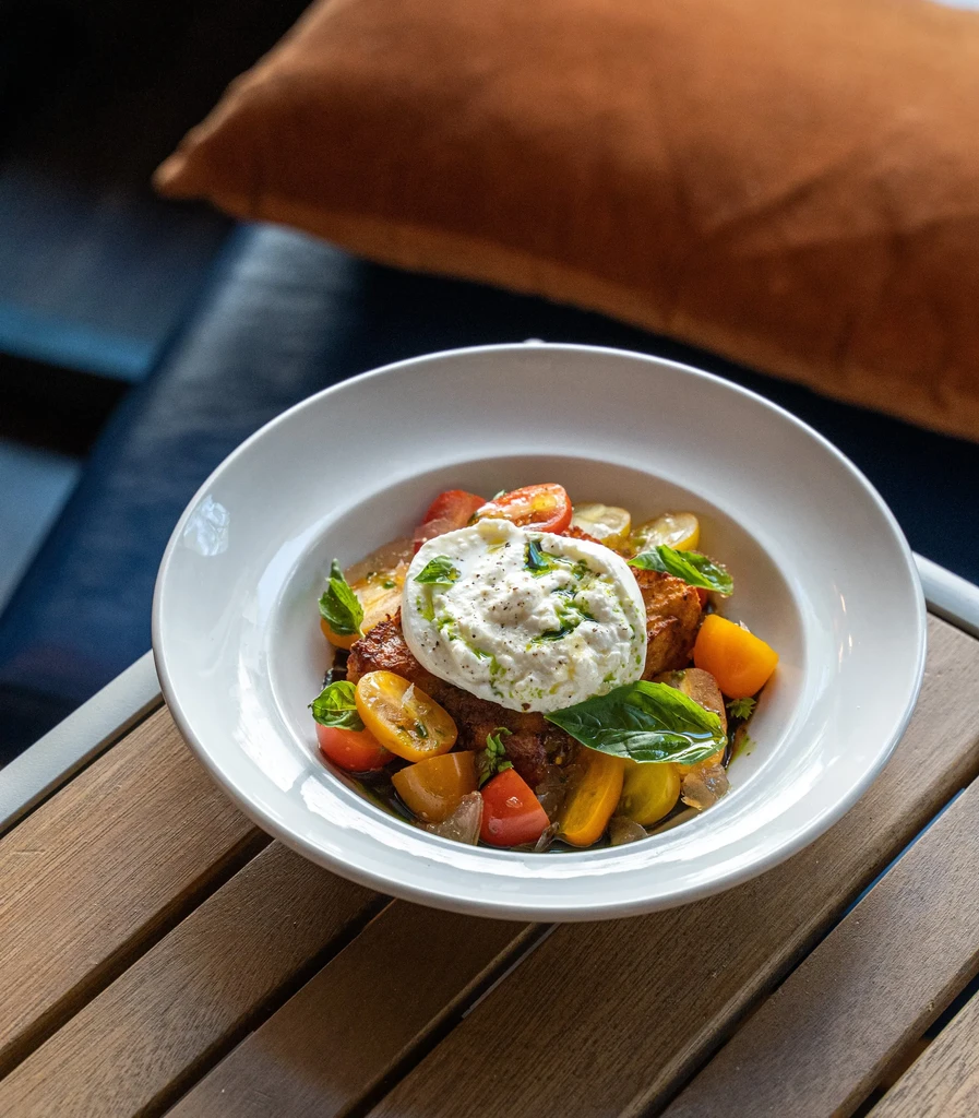 Burrata with tomatoes, basil, green sauce, and pepper on toasted bread.