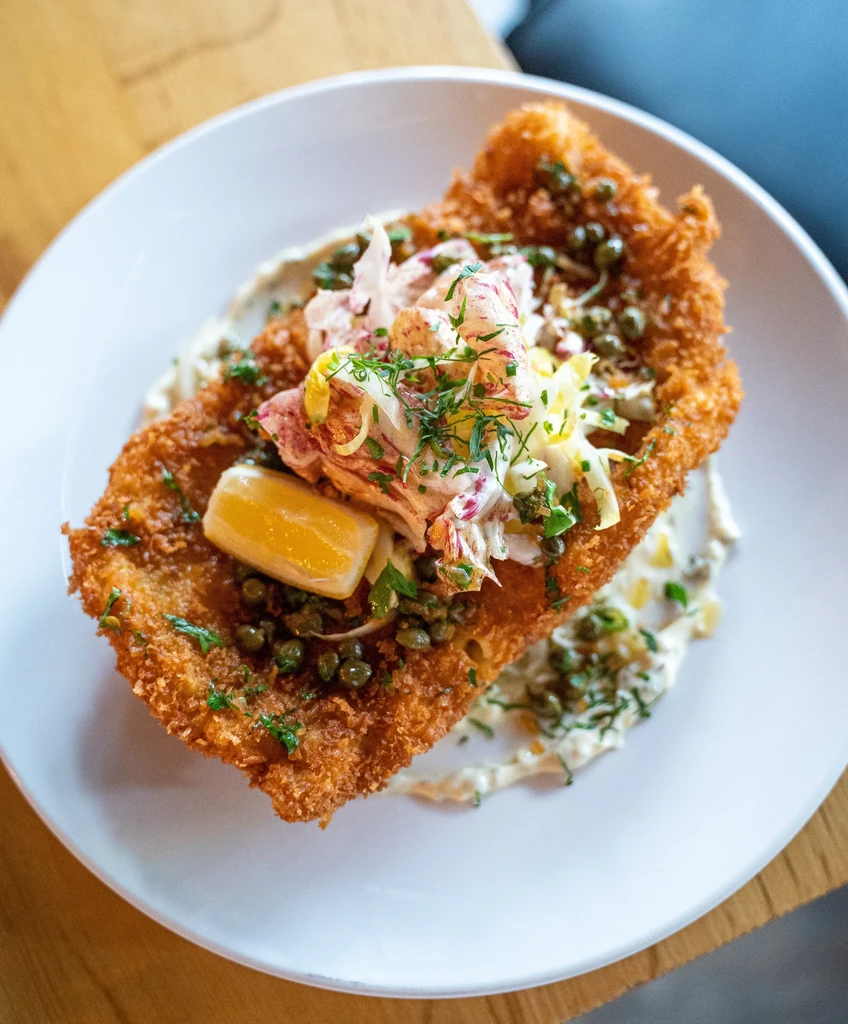 Plated fried schnitzel or fish with slaw, lemon, capers, and creamy sauce.