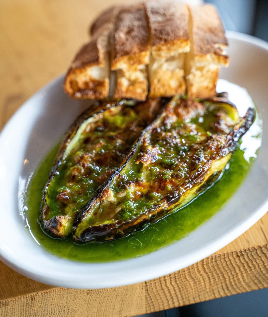 Grilled vegetables with green pesto sauce in a white bowl.
