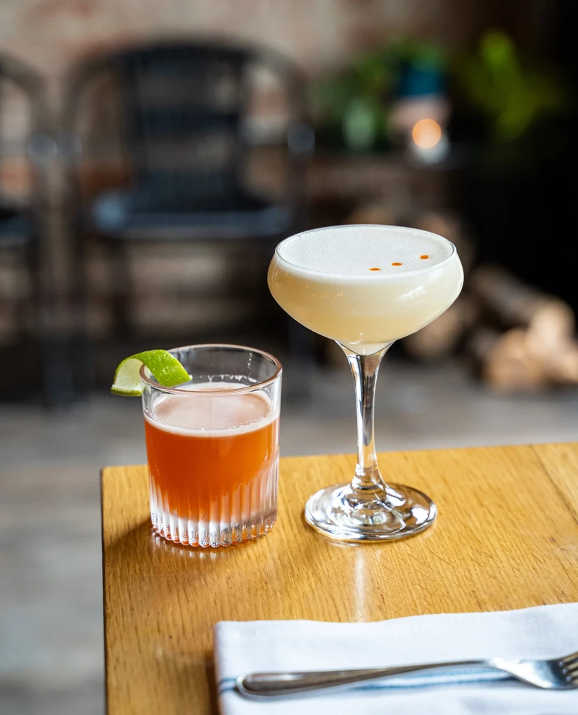 Two cocktails: orange with lime peel, yellow frothy with orange drops.