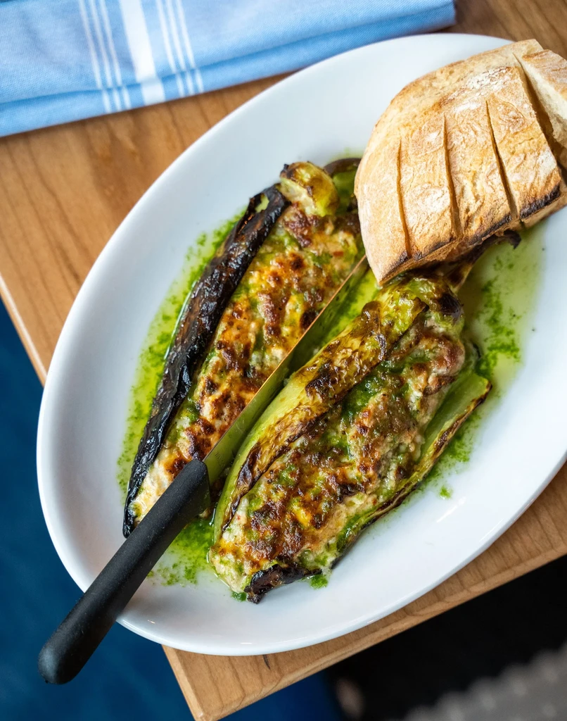 Two golden-brown stuffed vegetables in vibrant green sauce with bread.