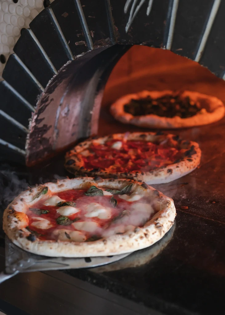 Bubbling Margherita pizza and two others baking in a wood oven.