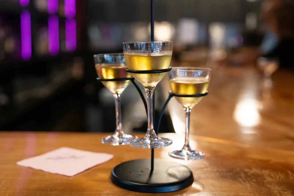 Drink flight in metal stand on wooden bar, with purple light.