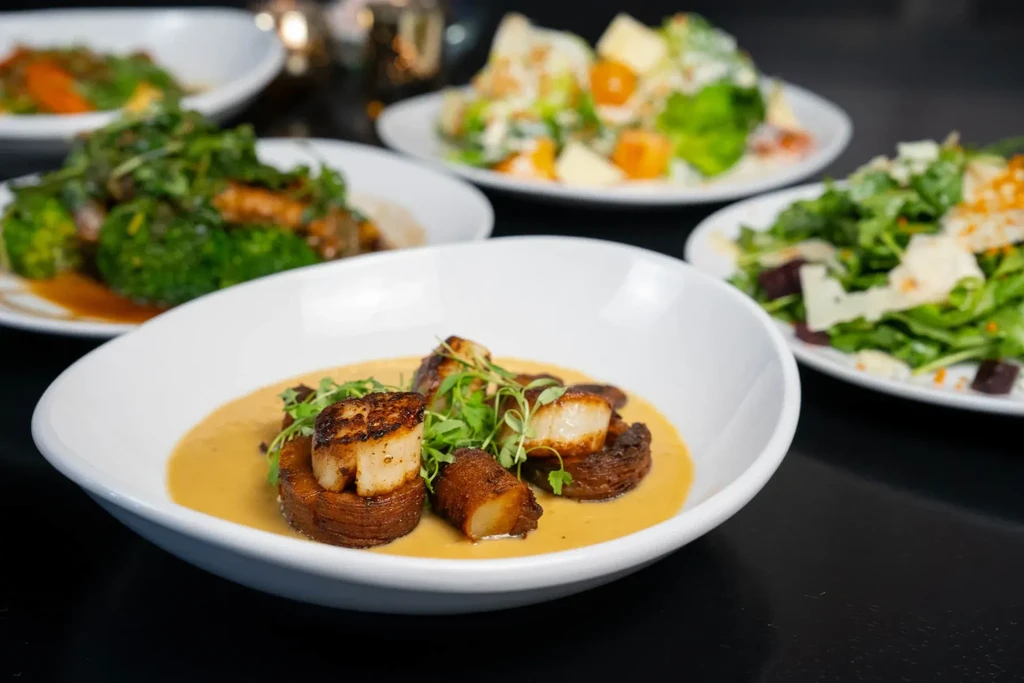 Seared scallops in a bowl surrounded by other gourmet dishes.