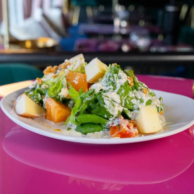 Fresh salad with creamy dressing, fruit, nuts, on pink surface.
