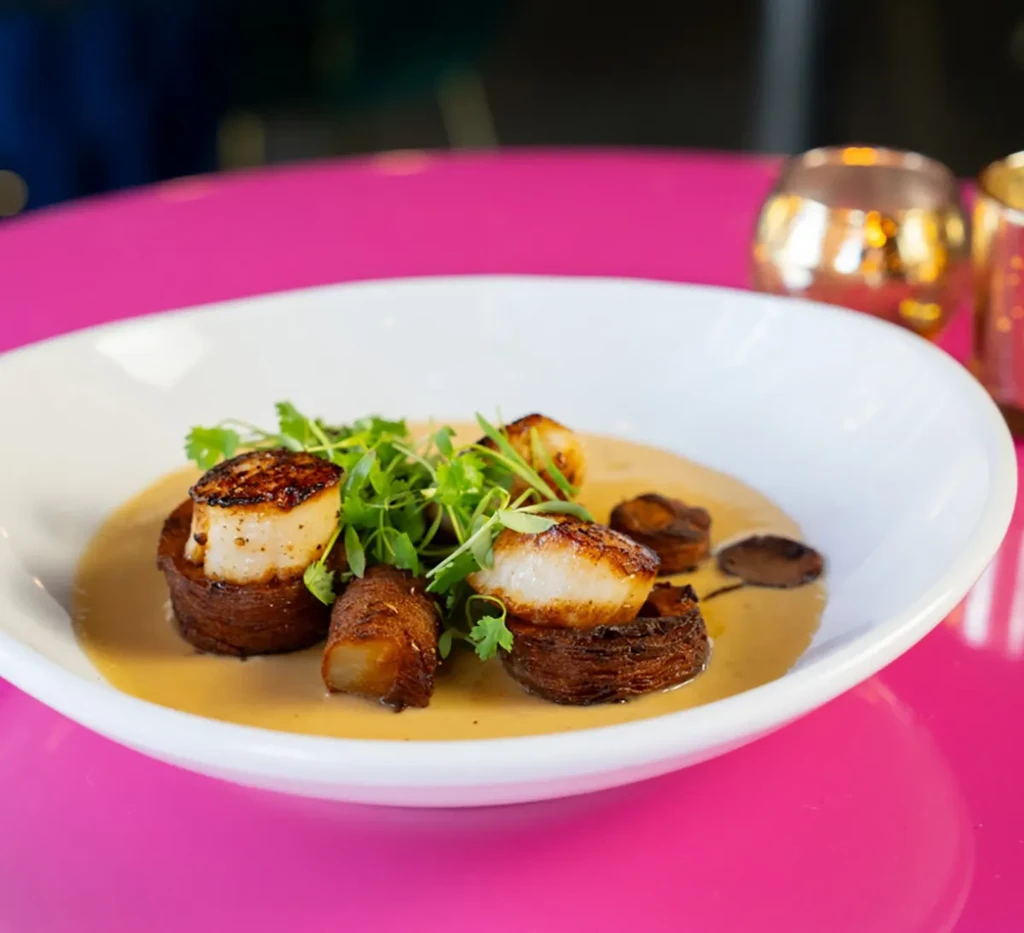 Three seared scallops on crispy disks with sauce and herbs.