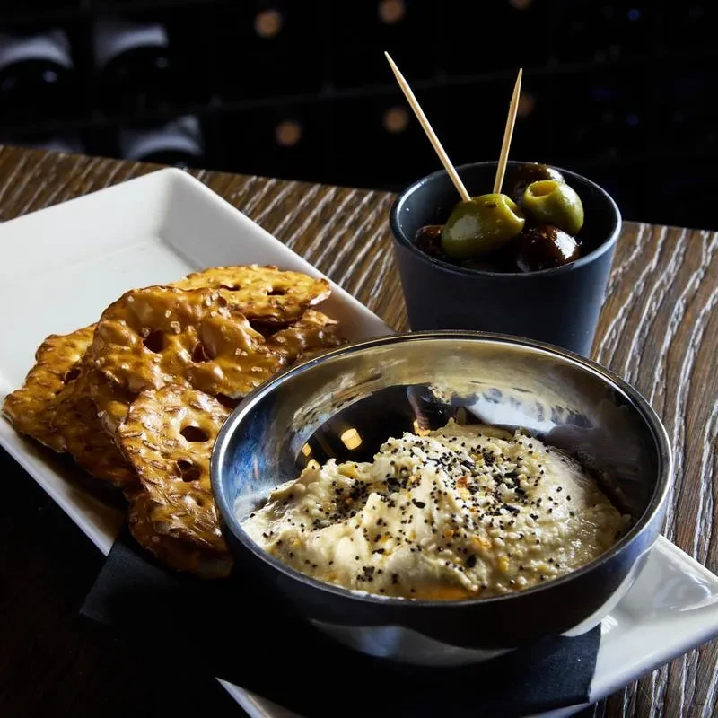 Appetizer spread: seeded dip, pretzel crisps, and olives on a table.