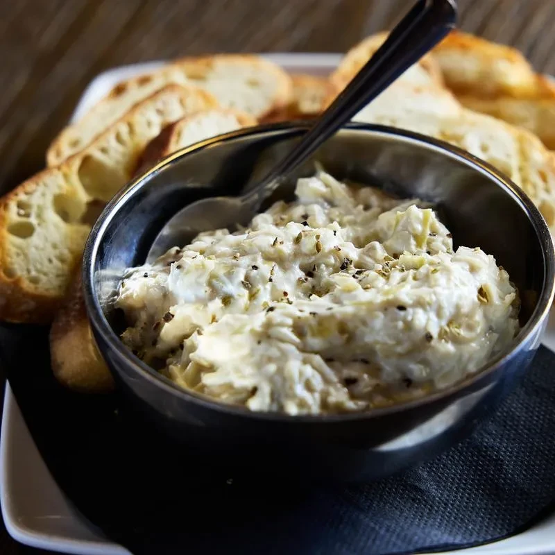 Creamy, herbed dip in metal bowl with spoon and toasted bread.