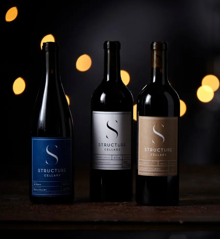 Three wine bottles with varied labels on a rustic wood surface.
