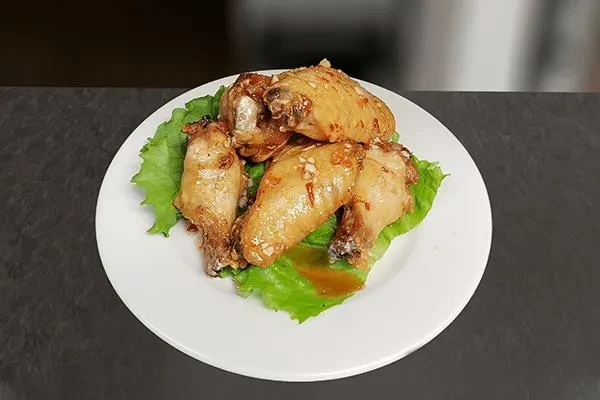 Golden-brown glazed chicken wings garnished with lettuce on a white plate.