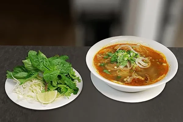 Close-up of Vietnamese noodle soup with reddish broth and fresh herbs.