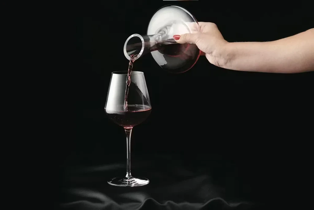 Red wine streams from a decanter into a stemmed wine glass.