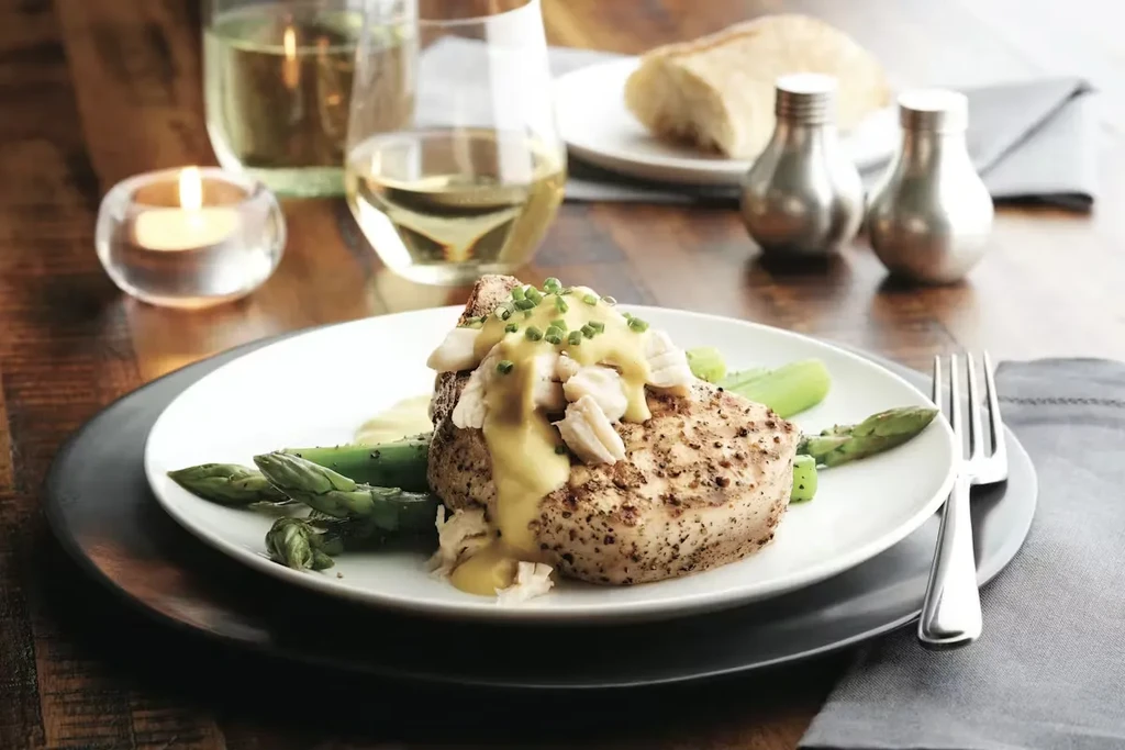 Grilled fish with crab, asparagus, sauce, and wine on a rustic table.