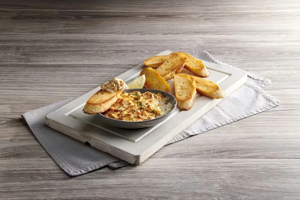 Baked dip with herbs, lemon, and toasted baguette on a cutting board.