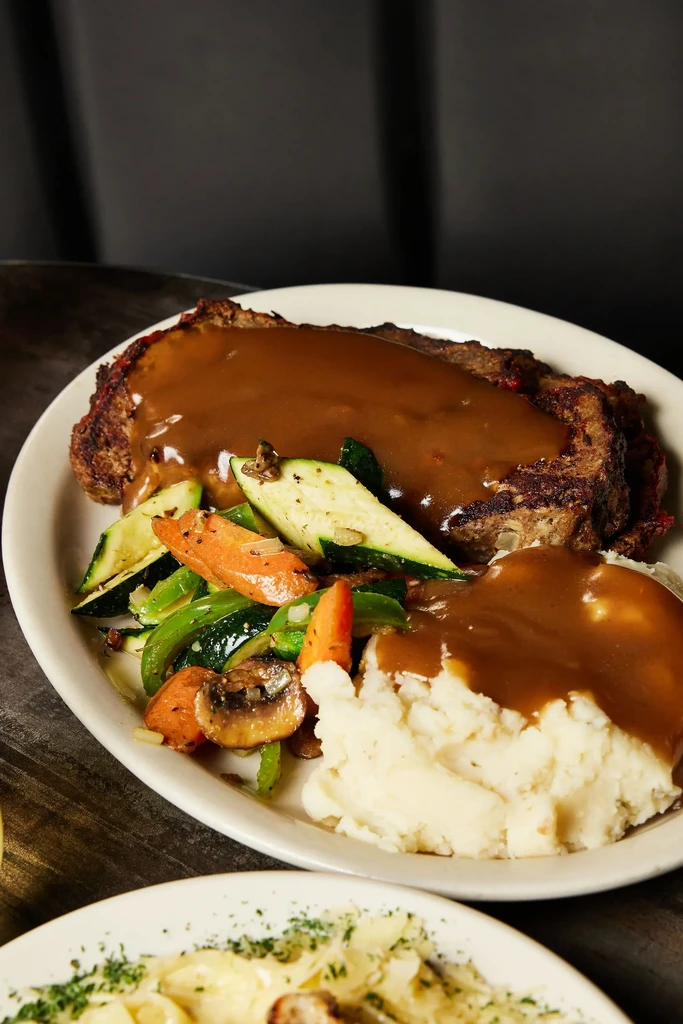 Meatloaf with gravy, mashed potatoes, and vegetables on a white plate.
