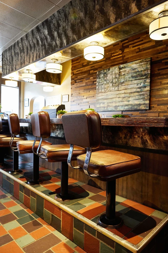 Brown retro bar stools at a modern diner counter with geometric tiles.