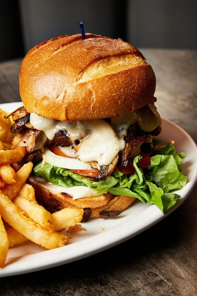 Stacked gourmet burger with melted cheese and crispy fries on a white plate.