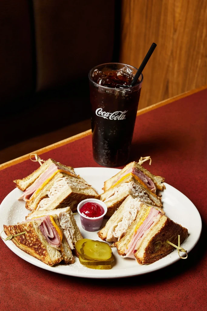 Plate of classic club sandwiches, pickles, red sauce, and Coca-Cola.