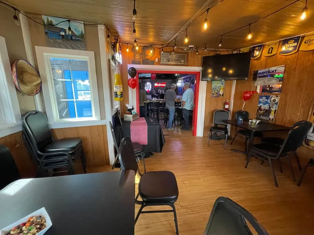 Warmly lit casual restaurant interior with beer posters, stacked tables, and people.