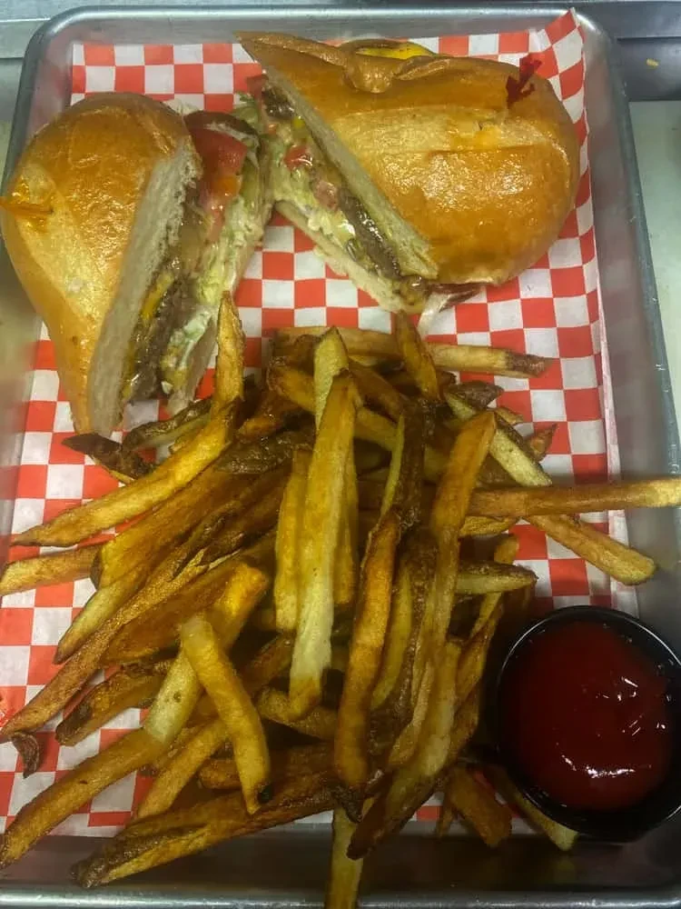 Large sliced sandwich, fries, and ketchup on checkered paper.
