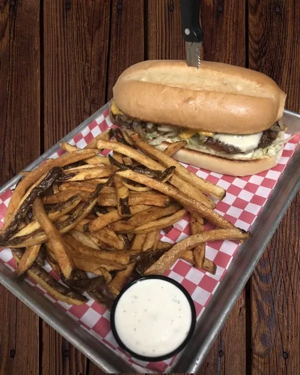 Large sandwich with knife, fries, and sauce on a checkered tray.