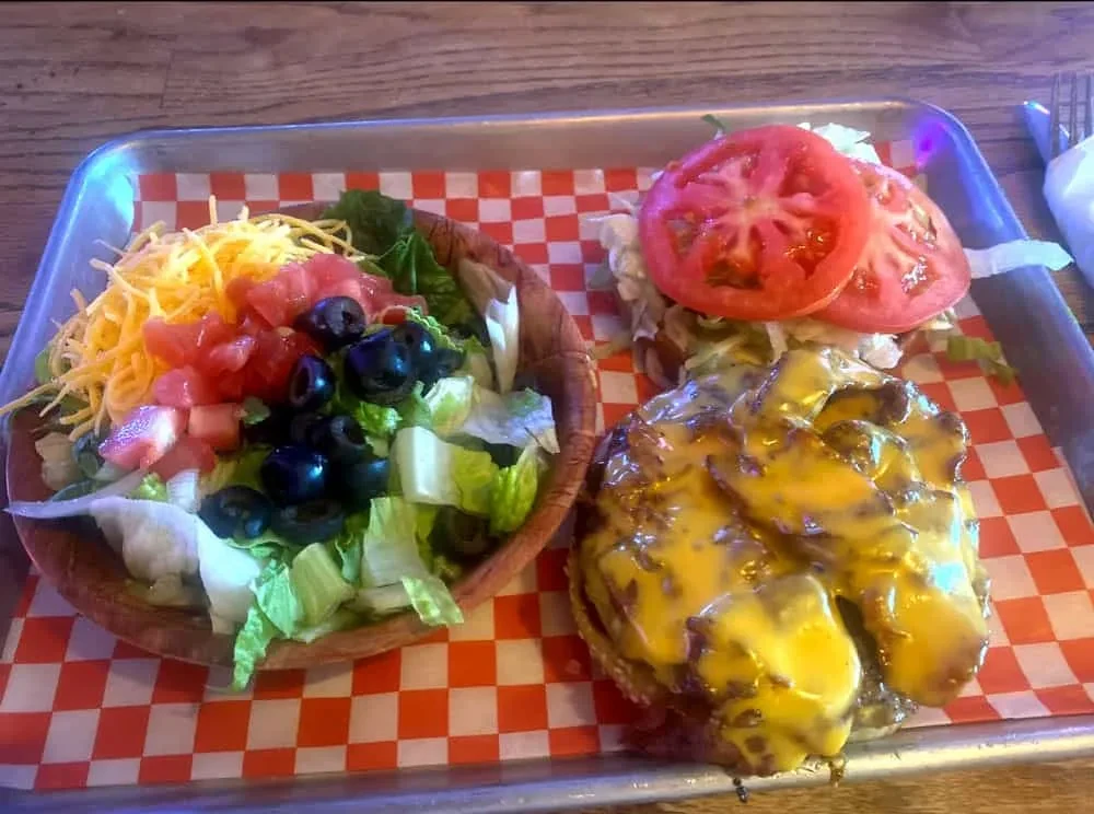 Open-faced burger and salad in tortilla bowl served on a metal tray.