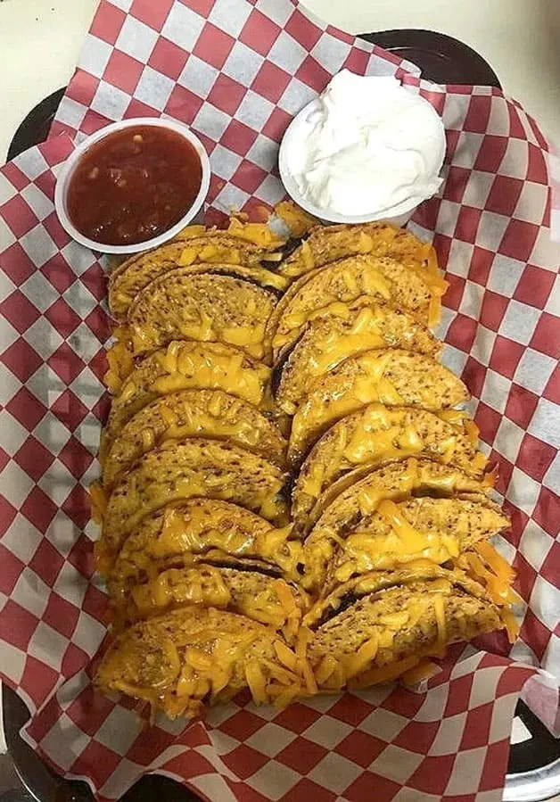 Basket of crispy mini tacos with melted cheese, salsa, and sour cream.