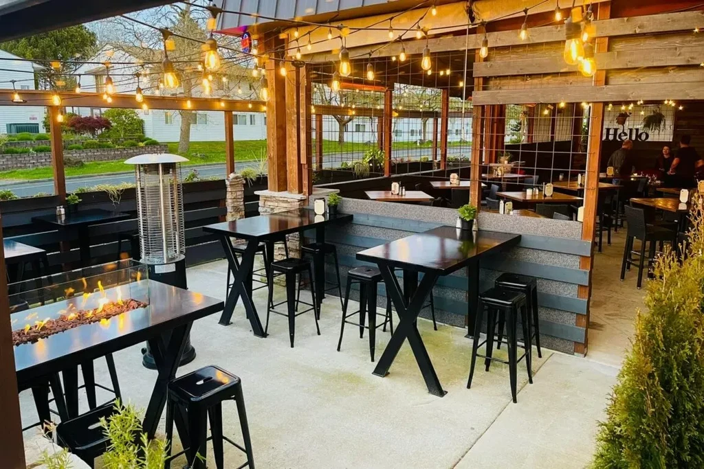 Modern restaurant patio with fire pit table, high-tops, and string lights.