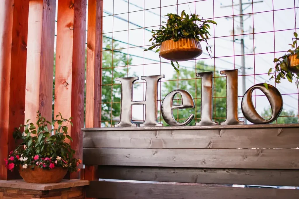 Metallic 'HELLO' sign on a wooden ledge with patio plants.