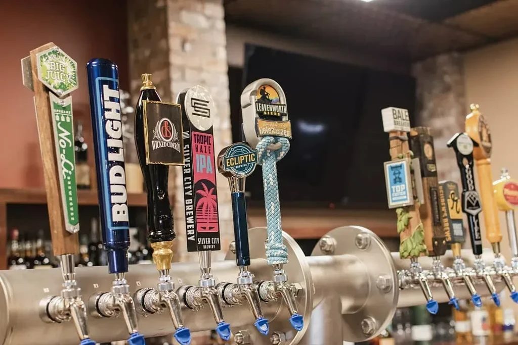 Close-up of many branded beer tap handles on a stainless steel draft system.
