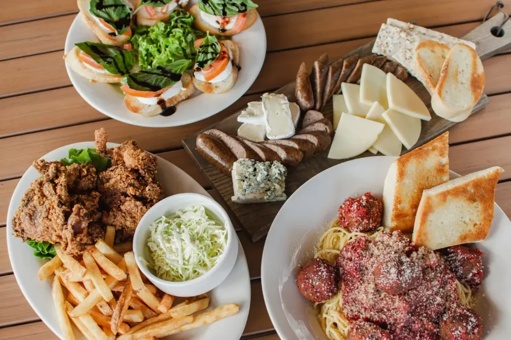 A spread of bruschetta, fried chicken, spaghetti, charcuterie on wood.