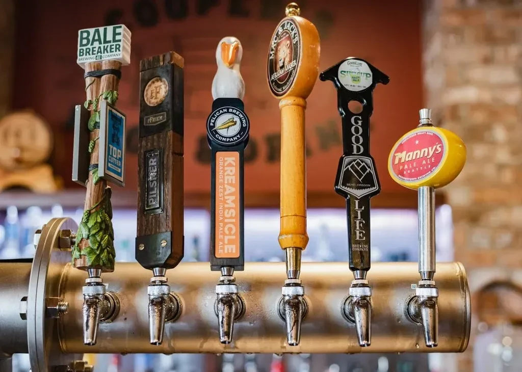 Six unique brewery tap handles on a polished metal bar.