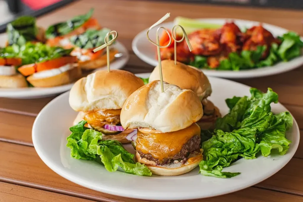 Three plates of appetizers: mini cheeseburger sliders, bruschetta, and chicken wings.