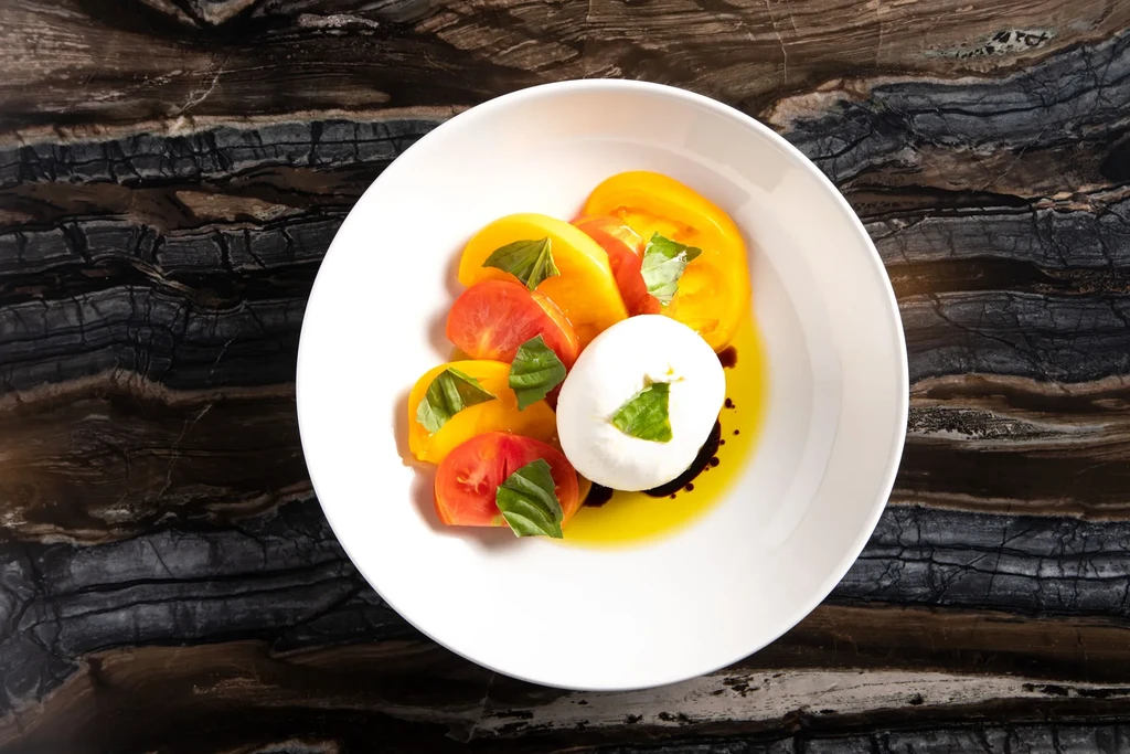 Beautifully plated heirloom tomato, mozzarella, basil, balsamic salad on dark stone.