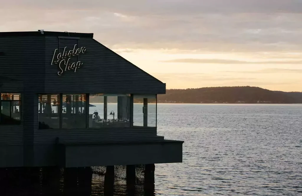 Neon-signed Lobster Shop restaurant on stilts over water at twilight.