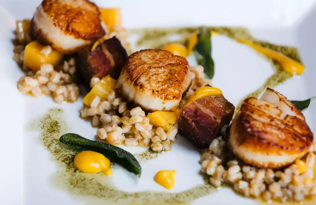 Three seared scallops atop grains, bacon, green and yellow sauces.