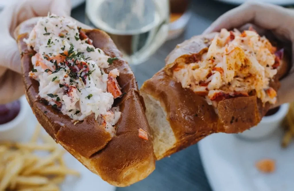 Two hands holding generously filled lobster rolls with golden-brown buns.