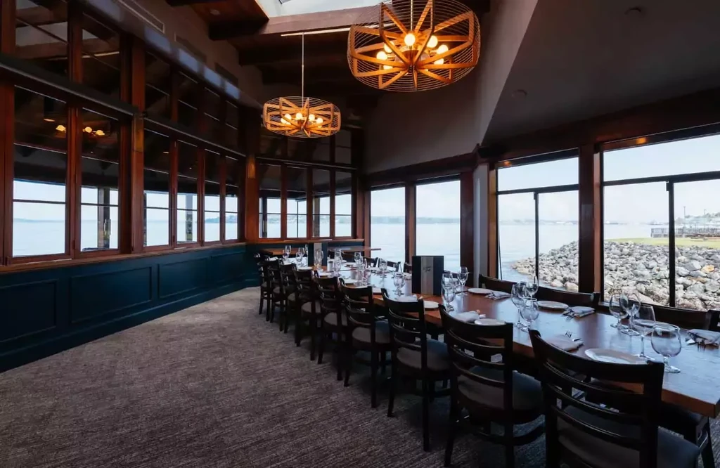 Elegant private dining room with long table, modern chandeliers, and water view.