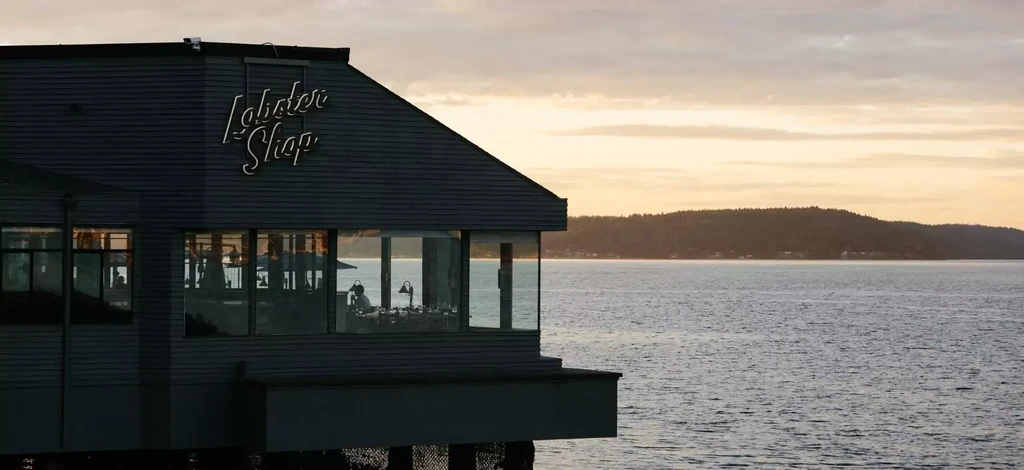 Neon "Lobster Shop" building on pilings over water at sunset.