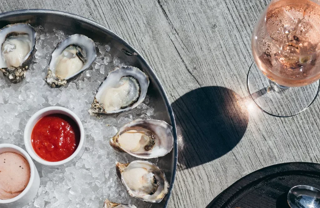 Six fresh oysters on ice with sauces and rosé wine.