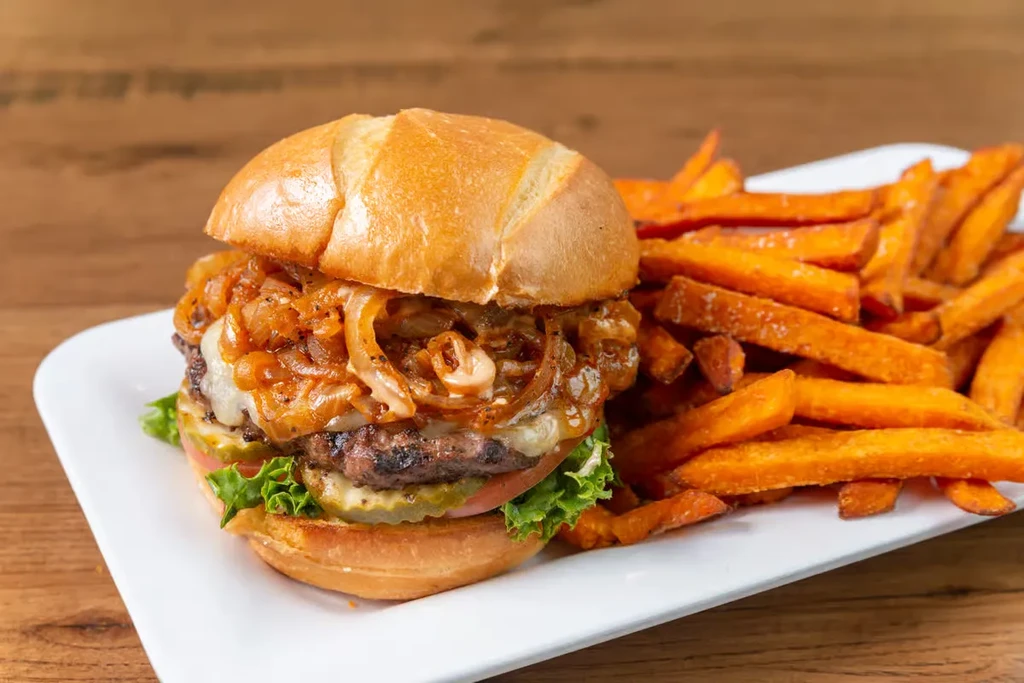 Close-up of burger with caramelized onions and sweet potato fries.