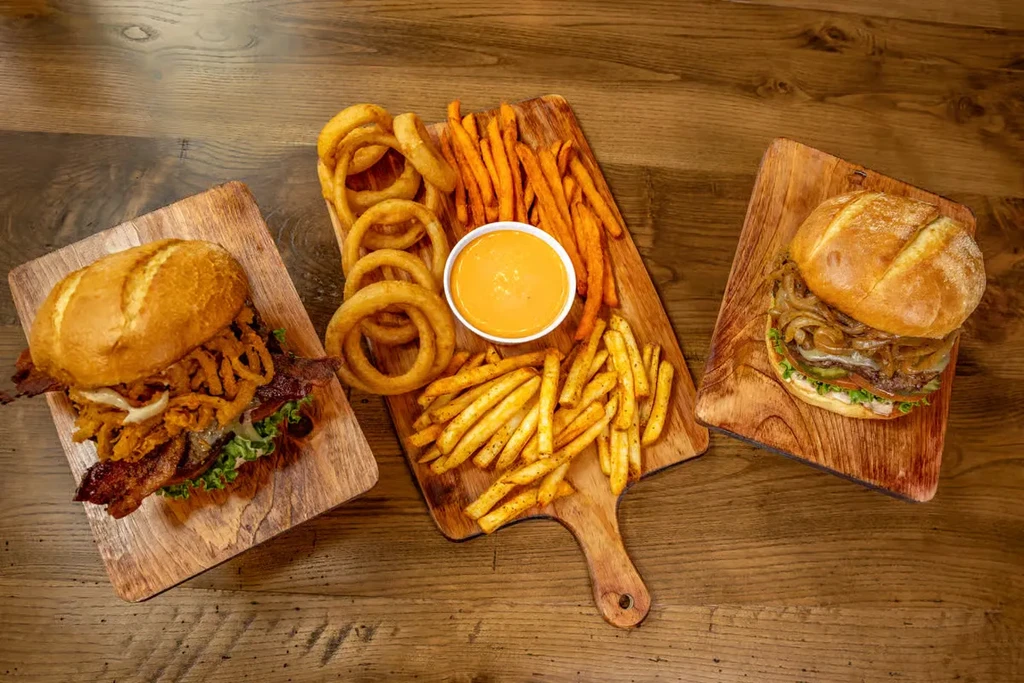 Overhead: Two burgers and assorted fried sides on a rustic wooden table.