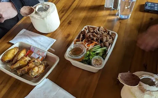Top-down: Chicken wings, Vietnamese vermicelli, coconuts on wooden table.