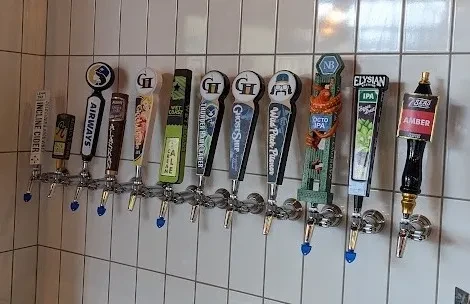 Ten unique beer and cider tap handles on a white tiled wall.