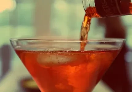 Orange beverage poured into a martini glass with ice.