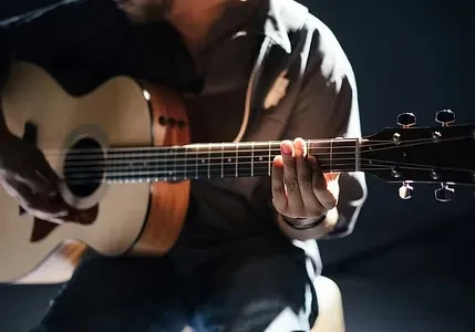 Hands playing a light wood acoustic guitar under stage lights.