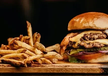 Double cheeseburger with melted cheese and rustic fries on wood.