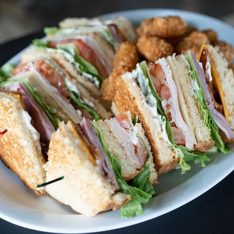 Quartered club sandwiches and potato croquettes on a white oval plate.